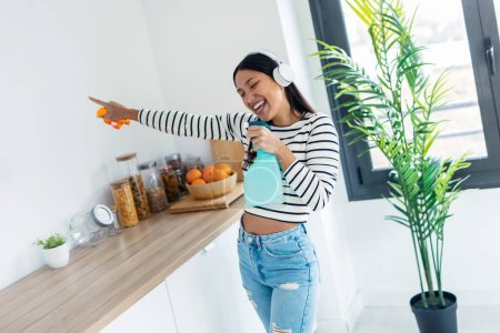Téléchargez les photos : Tourné de belle femme heureuse chantant et dansant tout en nettoyant la cuisine à la maison - en image libre de droit