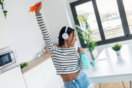 Foto de Foto de hermosa mujer feliz cantando y bailando mientras se limpia la cocina en casa - Imagen libre de derechos
