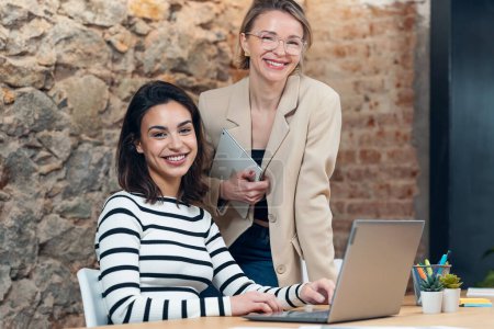 Téléchargez les photos : Prise de vue de deux belles femmes de créateurs travaillant avec un ordinateur portable tout en choisissant des matériaux dans la tablette numérique dans le bureau moderne. - en image libre de droit