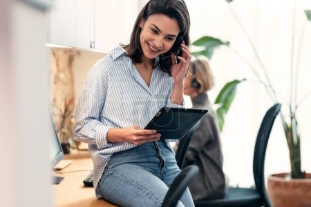 Téléchargez les photos : Prise de vue d'un bel opérateur féminin parlant avec un casque sans fil tout en regardant sur une tablette numérique au bureau - en image libre de droit