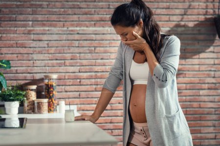 Photo for Shot of tired disgusted pregnant woman with nausea while eating a yogurt in the kitchen at home - Royalty Free Image