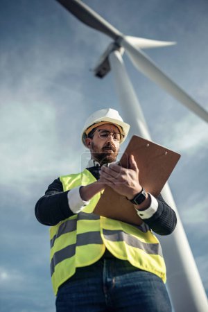 Shot of mature male engineer checking while taking notes of wind turbines operation