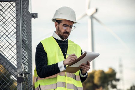 Photo for Shot of mature male engineer checking while taking notes of wind turbines operation - Royalty Free Image