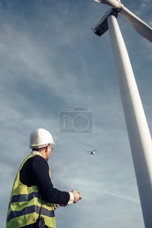 Téléchargez les photos : Vidéo d'hommes d'âge mûr ingénieurs volant un drone au-dessus du champ de l'éolienne tout en vérifiant que tout est correct - en image libre de droit