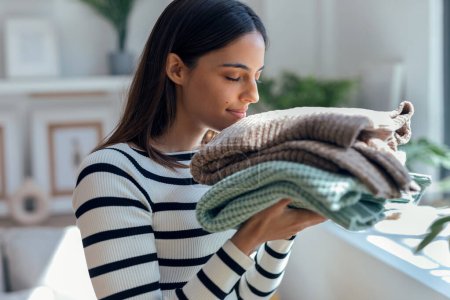 Shot of beautiful woman smelling clean laundry after folding in living room at home