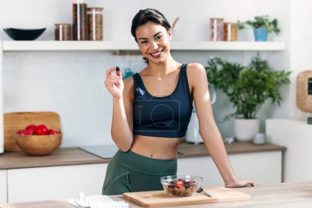 Shot of athletic woman eating a healthy bowl of muesli with fruit in the kitchen at home