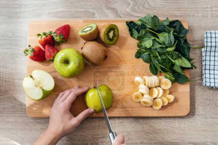 Téléchargez les photos : Gros plan des mains de femme coupant des fruits et légumes dans la cuisine à la maison - en image libre de droit