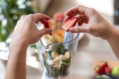 Foto de Primer plano de las manos de la mujer preparando smothie con verduras y frutas en la cocina en casa. - Imagen libre de derechos