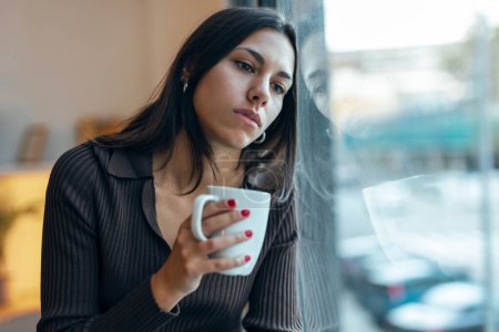 Photo for Shot of beautiful thoughtful woman drinking a cup of coffee while looking forward next to the window at home - Royalty Free Image