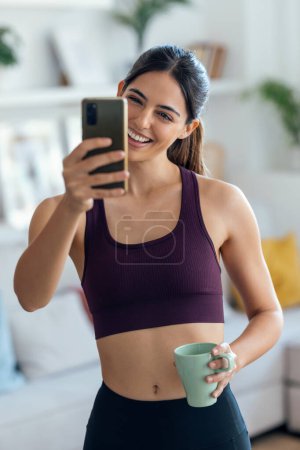 Téléchargez les photos : Tourné d'une femme sportive faisant un vidéocall avec son smartphone tout en buvant du café à la maison. - en image libre de droit