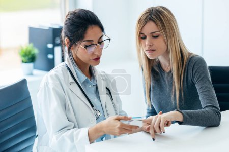 Foto de Inyección de una hermosa doctora midiendo el corazón y la presión arterial mientras cuida a un paciente joven en la consulta médica - Imagen libre de derechos
