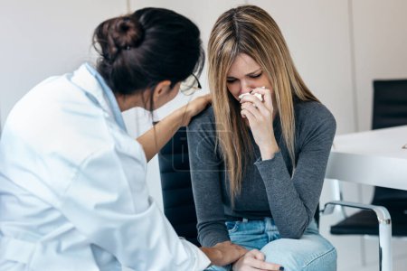 Foto de Foto de hermosa mujer preocupada llorando mientras hacía terapia con su psicóloga en la consulta médica - Imagen libre de derechos