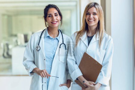 Portrait of two attractive female doctors smiling while looking at camera standing in medical consultation