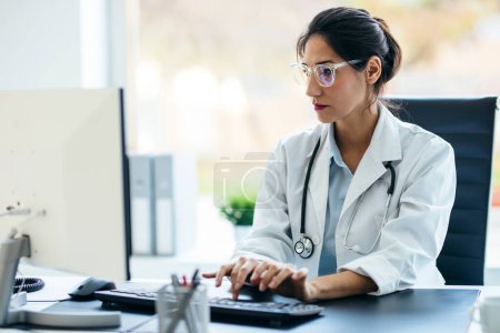 Téléchargez les photos : Prise de vue de belle femme médecin travaillant avec ordinateur en consultation médicale. - en image libre de droit