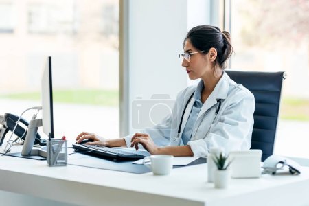 Tiro de hermosa doctora trabajando con computadora en consulta médica.