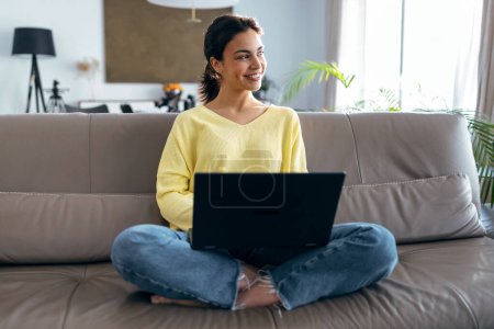 Téléchargez les photos : Prise de vue de belle jeune femme travaillant avec son ordinateur portable tout en étant assis sur un canapé à la maison. - en image libre de droit
