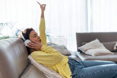 Téléchargez les photos : Prise de vue de femme détendue écoutant de la musique avec smartphone alors qu'elle était allongée sur le canapé à la maison. - en image libre de droit