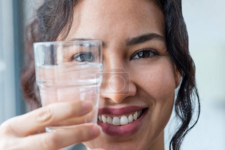 Photo for Close up of beautiful sporty woman drinking a glass of water while standing near the window at home - Royalty Free Image