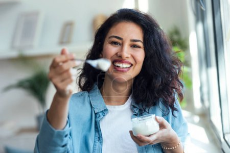 Photo for Portrait of beautiful smiling woman having fun while feeding yogurt to camera at home - Royalty Free Image