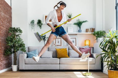 Photo for Shot of funny motivated woman dancing and listening to music with headphones while sweeping the house - Royalty Free Image