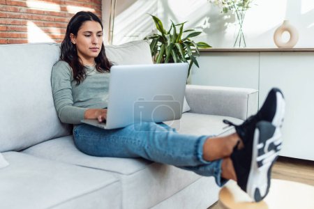 Foto de Foto de una hermosa mujer joven que trabaja con su computadora portátil mientras está sentada en un sofá en casa. - Imagen libre de derechos