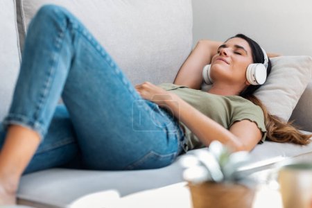 Téléchargez les photos : Prise de vue de belle femme gentille se détendre tout en écoutant de la musique avec des écouteurs couchés sur le canapé à la maison - en image libre de droit