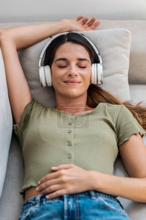Téléchargez les photos : Prise de vue de belle femme gentille se détendre tout en écoutant de la musique avec des écouteurs couchés sur le canapé à la maison - en image libre de droit