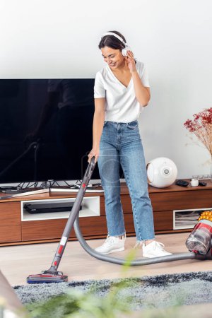 Téléchargez les photos : Prise de vue de jeune femme heureuse écoutant de la musique tout en nettoyant le sol du salon avec un nettoyant vaccinal - en image libre de droit
