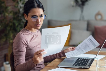 Téléchargez les photos : Prise de vue de belle jeune femme regardant des papiers tout en travaillant avec PC - en image libre de droit