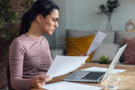Photo for Shot of beautiful young woman looking at papers while working with pc - Royalty Free Image