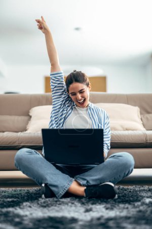 Photo for Shot of pretty woman celebrating something while working with laptop sitting on a the floor at home. - Royalty Free Image