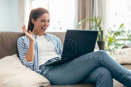 Foto de Fotografía de la hermosa mujer feliz haciendo videollamada mientras está sentado en un sofá en la sala de estar en casa - Imagen libre de derechos