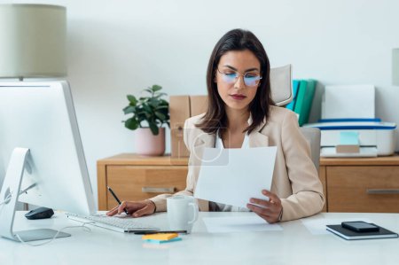 Photo for Shot of elegant smart business woman working with computer while reading some notes in the office - Royalty Free Image