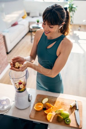 Téléchargez les photos : Tourné de belle femme sportive faisant smoothie sain tout en écoutant de la musique dans la cuisine. - en image libre de droit
