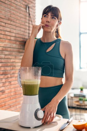 Photo for Shot of beautiful sporty woman doing healthy smoothie while listening to music in the kitchen. - Royalty Free Image