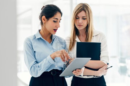 Téléchargez les photos : Prise de vue de deux élégantes femmes d'affaires attrayantes travaillant avec une tablette numérique tout en parlant dans une start-up moderne - en image libre de droit