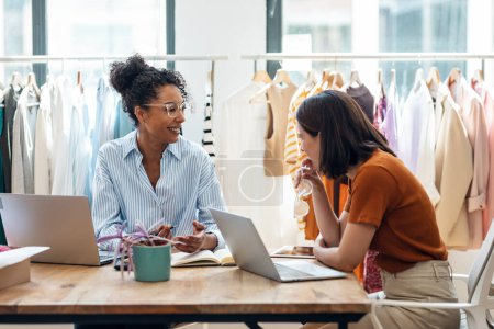 Photo for Shot of two fashion designers working with laptop and deciding details of clothes new collection in the sewing workshop. - Royalty Free Image