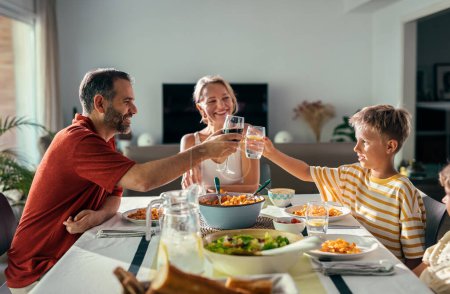 Téléchargez les photos : Tourné de belle famille aimable toasting tout en mangeant ensemble dans la cuisine à la maison - en image libre de droit