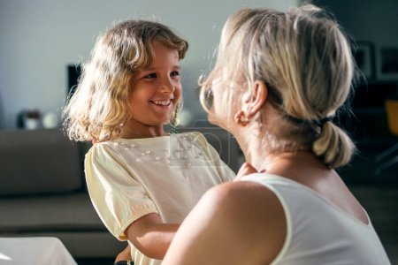 Aufnahme einer glücklichen Mutter beim Spielen und Umarmen ihrer schönen Tochter im heimischen Esszimmer