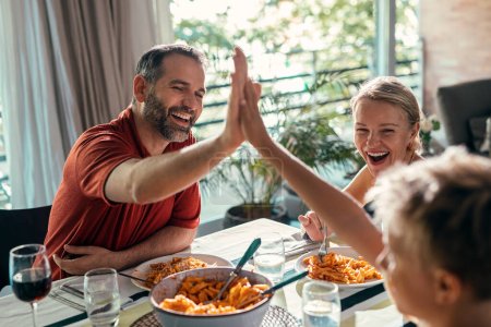Aufnahme einer schönen netten Familie, die feiert und Hände schüttelt, während sie zu Hause gemeinsam in der Küche isst