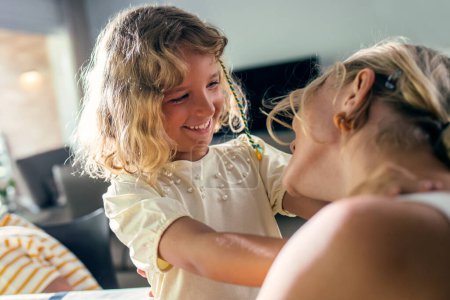 Téléchargez les photos : Tourné de mère heureuse jouant et embrassant sa belle fille dans la salle à manger à la maison - en image libre de droit