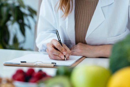 Photo for Close up of beautiful smart nutritionist woman taking notes in the nutritionist consultation - Royalty Free Image