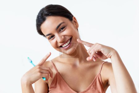 Téléchargez les photos : Prise de vue de jolie jeune femme se brossant les dents tout en regardant la caméra en blanc isolé - en image libre de droit