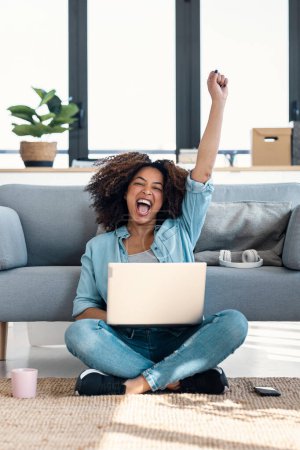 Shot of beautiful woman celebrating something while working with laptop sitting on the home