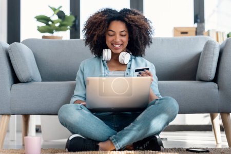 Foto de Tiro de mujer relajante que paga algo en línea con su tarjeta de crédito con el ordenador portátil mientras está sentado en el suelo en la sala de estar en casa - Imagen libre de derechos