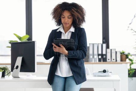Téléchargez les photos : Prise de vue de femme d'affaires élégante travaillant avec une tablette numérique tout en étant assis sur un bureau dans un bureau moderne - en image libre de droit