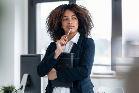 Foto de Foto de elegante hermosa mujer de negocios mirando hacia adelante mientras sostiene una tableta digital en una oficina moderna - Imagen libre de derechos