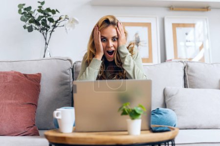 Photo for Shot of pretty surprised woman celebrating something while working with laptop sitting on a couch at home - Royalty Free Image