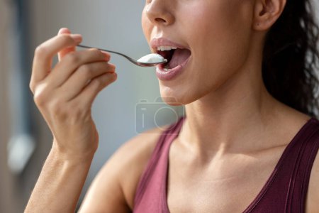 Photo for Close up of beautiful sporty woman eating yogurt while looking forwards through the window at home. - Royalty Free Image