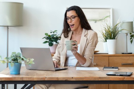 Téléchargez les photos : Prise de vue de femme d'affaires surprise travaillant avec un ordinateur portable tout en buvant du café dans le salon à la maison. - en image libre de droit
